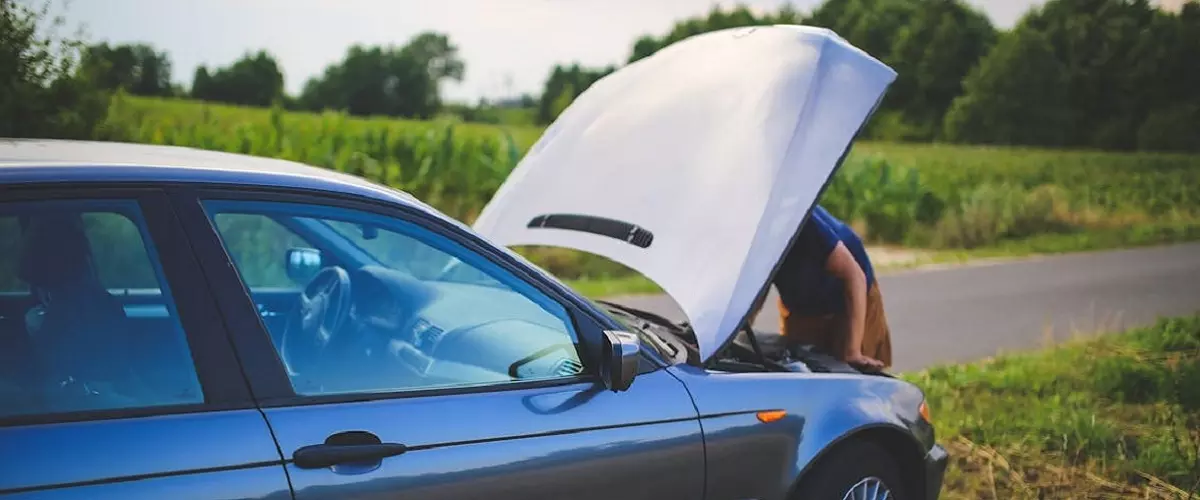 Hombre revisando el motor de un auto al costado de la ruta.